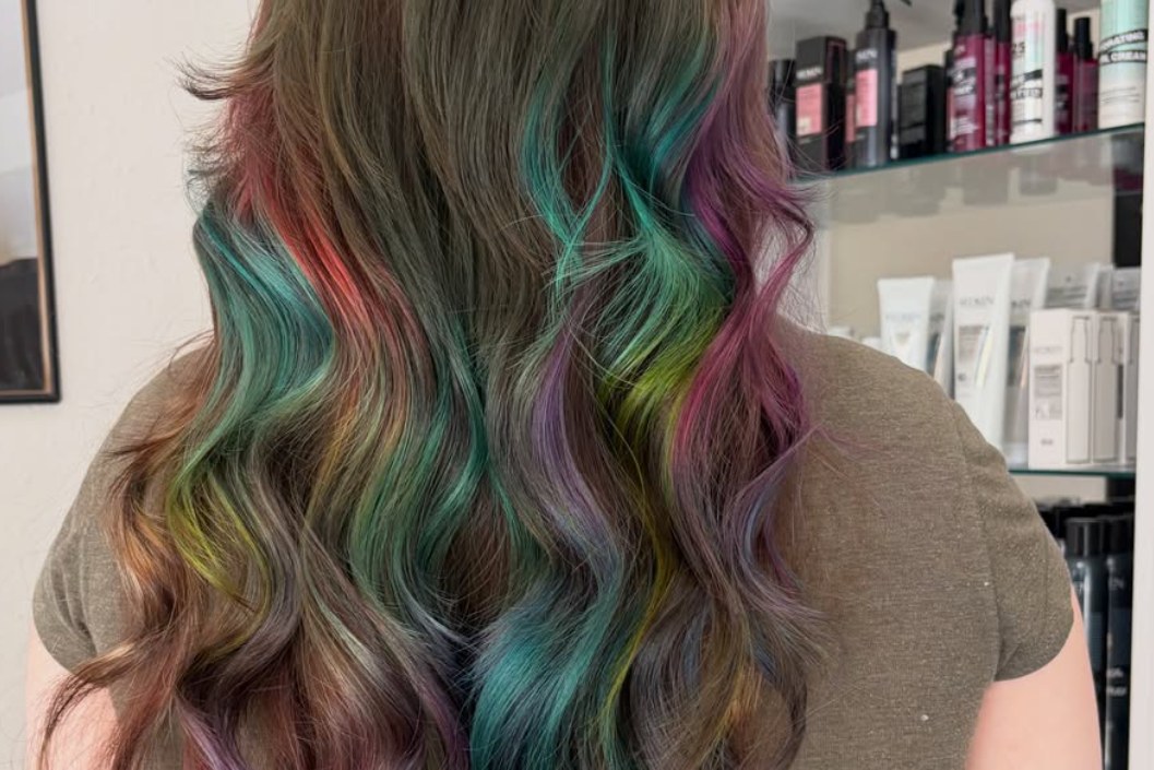 Long brown hair with vivid teal, purple, pink, and green color accents, photographed from behind